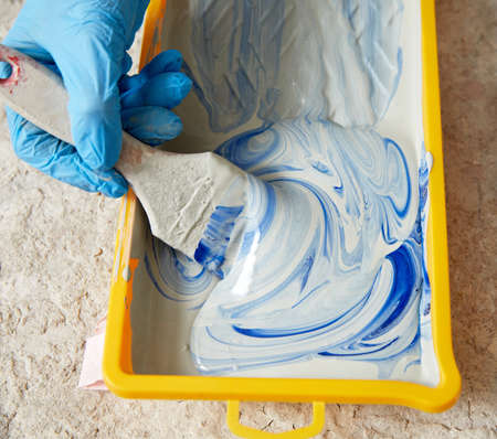 Cropped view of hand wearing gloves using paint brush and paintの写真素材