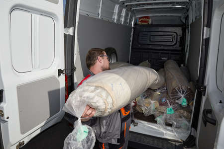 Worker standing near truck full of carpets. Cleaning service concept