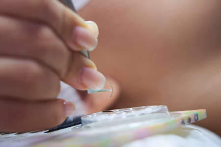 Eyelash Extension Procedure. Close-up of a master at work with artificial eyelash extensions material. Hand of master taking lashes from the setの写真素材