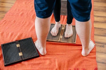 Man trainer helping woman to stand on sadhu yoga board, barefoot on a bed of nailsの写真素材