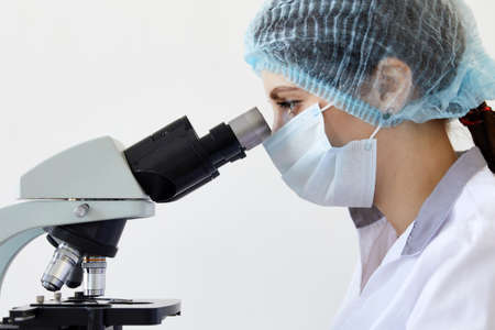 Female scientist looking through microscope in modern chemical laboratory doing some research....
