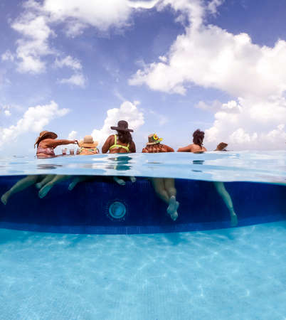 Half underwater split image of young women having fun in hotel pool in Caribbean sea. Concept of...