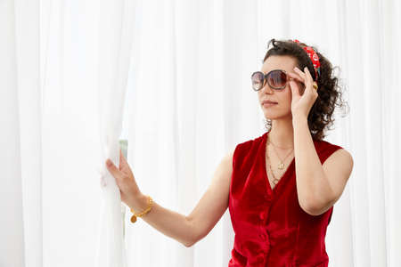 Beautiful young curly woman standing next to the curtains on big panoramic window