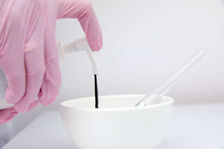 Close up of cosmetologist filling up a container with black face mask for carbon peeling