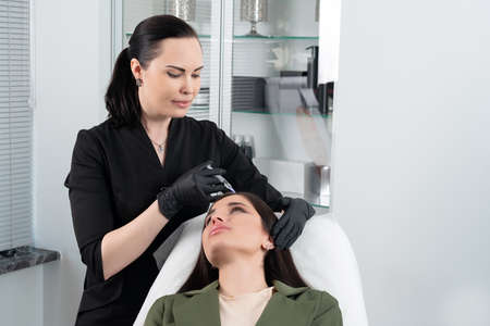 Young woman with hair problem receiving injection in head skin in a clinic. Mesotherapy treatment of hair loss, injection for hair growthの写真素材