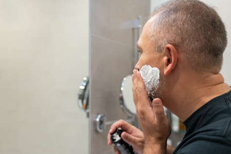 Mature handsome man applying shaving foam on his face to cut off his beard and mustache with razorの写真素材