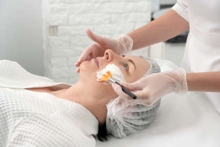 Mature woman receiving wwhte facial mask in spa beauty salon. Concept of skin care for older people