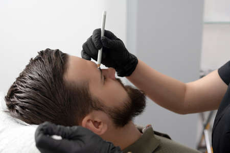 Portrait of a young handsome man with a wrinkled forehead. hands of a cosmetologist hold a cosmetic pencil and make marks on the guy faceの写真素材