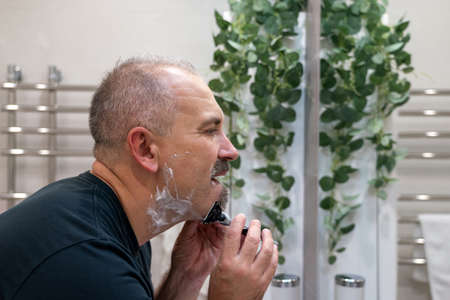 Middle aged handsome man shaving his beard in bathroom