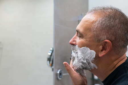 Mature handsome man applying shaving foam on his face to cut off his beard and mustache with razorの写真素材