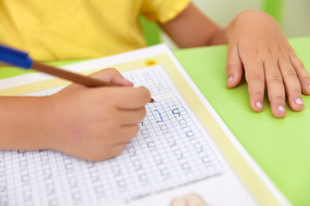 Hand of child holding pencil and study with learning writing number on paper book at school or kindergarten and nurseryの写真素材