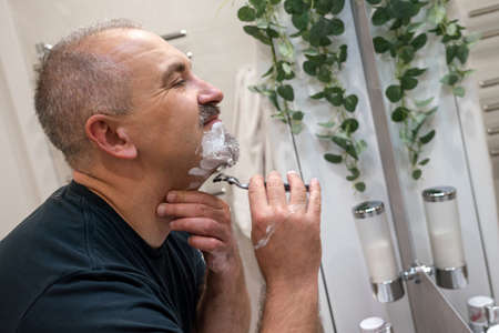 Man shaving with razor using foam in bathroom in the morning