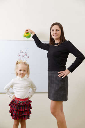 Teacher watering flower drawing on a white board with little girl standing near boardの写真素材