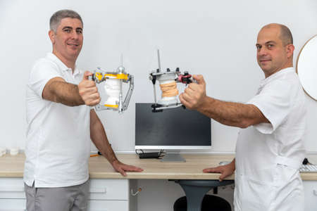 Two male dentists holding dental articulators in dental clinic