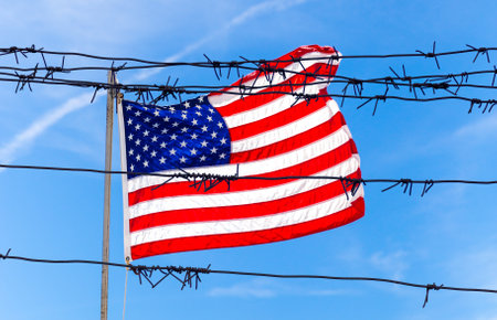 Barbed wire fence in front of Flag of United States of America waving in the windの写真素材