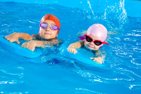 Two little girls having fun in pool learning how to swim using flutter boardsの写真素材