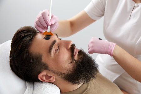 Cosmetologist applying a clay mask to male face. Spa treatment and face care in the beauty salon