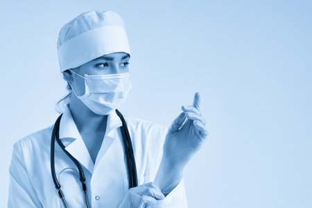 Young doctor putting on surgical gloves over white backgroundの写真素材