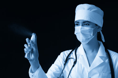 Young female doctor using spray antiseptic spray over black background with copy spaceの写真素材