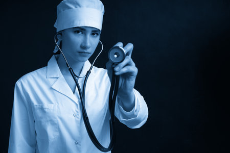 Cropped view of young female doctor holding stethoscope hanging on her neck, studio shot over black background with copy spaceの写真素材