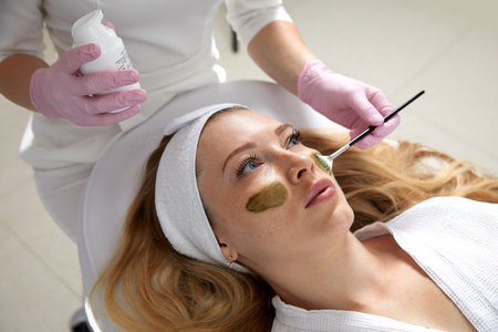 Cosmetologist applying a mask from clay to the face of a beautiful woman. Spa treatment and face care in the beauty salonの写真素材