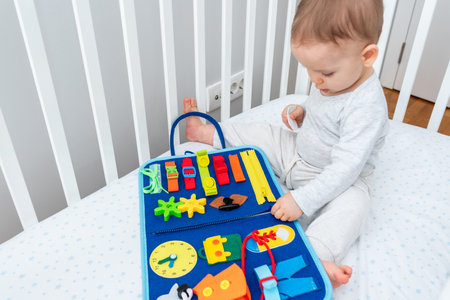 Baby playing with montessori quiet book sitting in a crib. Concept of smart books and modern...