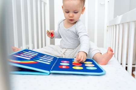 Baby playing with montessori busy book sitting in crib. Educational books and quiet books concept. Montessori busy boardの写真素材