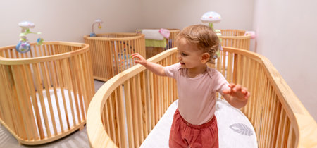 Happy toddler standing and playing in a stylish crib within a modern nursery filled with wooden...