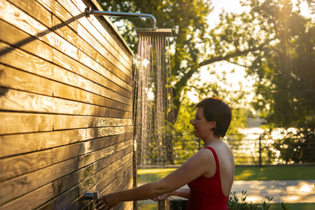 Smiling woman taking outdoor shower at sunset. Concept of refreshing summer relaxationの写真素材