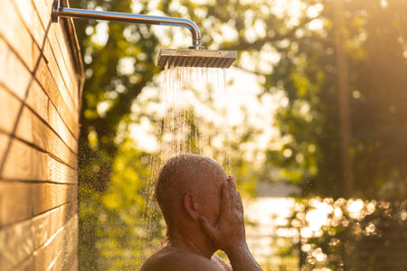 Man enjoying outdoor shower at sunset. Concept of evening relaxation and natural refreshmentの写真素材