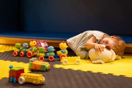 Tired sleepy toddler girl playing at beautiful daycare center with toys. Concept of daycare for babiesの写真素材