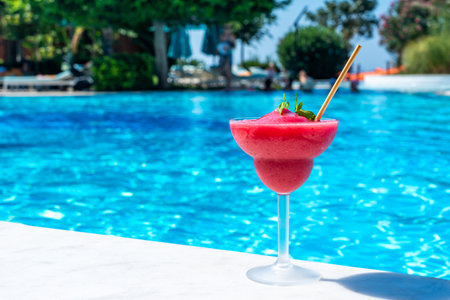 Frozen red drink by the pool on sunny day. Concept of refreshing summer poolside relaxationの写真素材