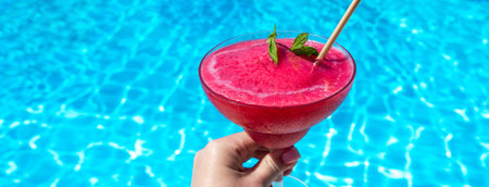 Frozen red drink held by pool on sunny day. Concept of summer refreshment and tropical leisureの写真素材