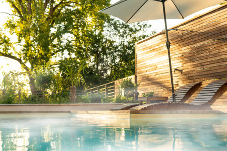 Outdoor poolside with loungers, umbrella, fog, and steam in sunny garden. Concept of peaceful relaxation and natural retreatの写真素材