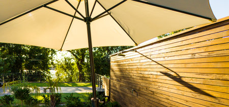 Sunlit outdoor umbrella and wooden fence with natural greenery. Concept of shade, privacy, and peaceful outdoor retreatの写真素材
