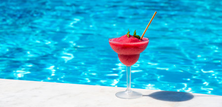 Frozen red cocktail by the blue pool on a sunny day. Concept of tropical refreshment and poolside relaxationの写真素材