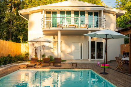 Modern villa with swimming pool and wooden deck in sunlight. Concept of luxury outdoor relaxation spaceの写真素材
