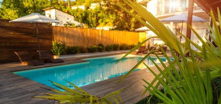 Swimming pool with wooden deck and green plants in sunlight. Concept of summer outdoor relaxationの写真素材