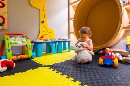 Young child sitting on soft play mats surrounded by toys and educational games in modern play areaの写真素材
