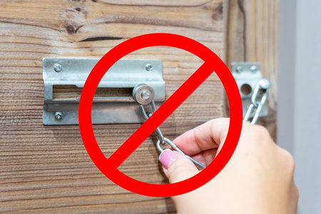 Hand unlocking chain door lock with red prohibition sign symbolizing restricted access or security alertの写真素材