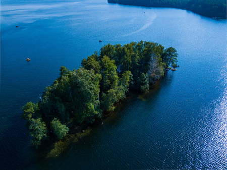Aerial drone view of piece of forest surrounded by water, mixed forest in the center of lake with floating boats around, Southern Ural - the land of lakes, Russiaの写真素材