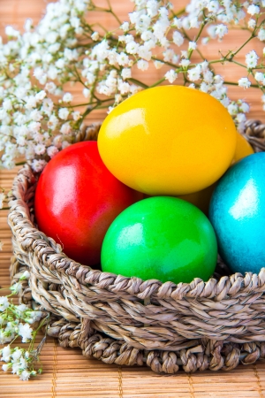 Colored painted eggs in a wattled basket with flowers の写真素材