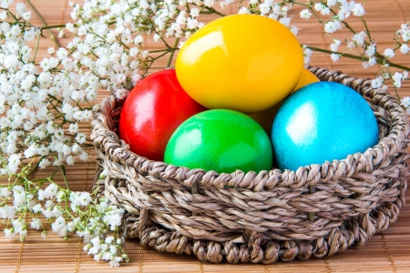Colored painted eggs in a wattled basket with flowers の写真素材