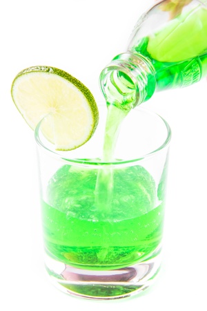 Tarragon green drink is poured from the bottle into a glass with lime on whiteの写真素材