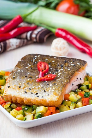 Fried fillet of red fish salmon with crispy skin, roasted vegetables, zucchini, pepper, beautiful dishの写真素材