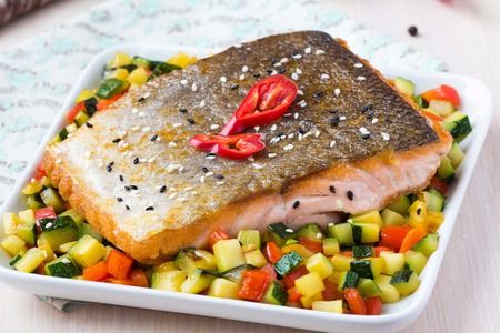 Fried fillet of red fish salmon with crispy skin, roasted vegetables, zucchini, pepper, beautiful dishの写真素材