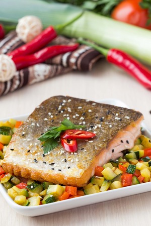 Fried fillet of red fish salmon with crispy skin, roasted vegetables, zucchini, pepper, beautiful dishの写真素材