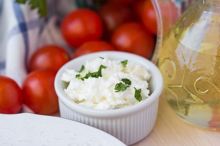 White soft cheese, feta, goat in bowl with tomatoes, parsley, olive oilの写真素材