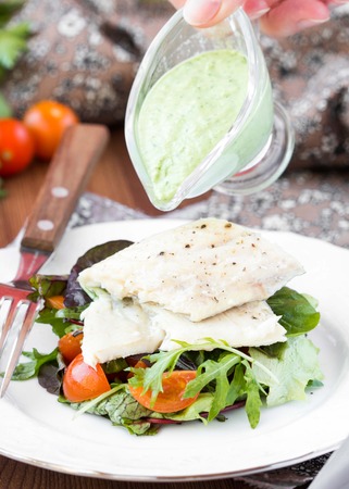 Fried white fish fillet with salad of lettuce, arugula, greens, tomatoes, green sauce with pea, parsleyの写真素材