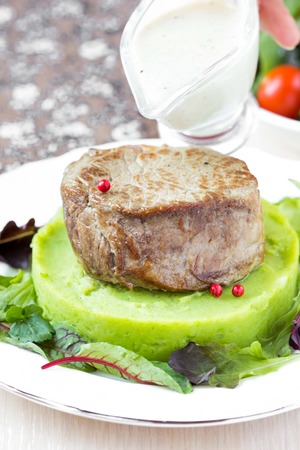 Grilled beef steak, green mashed potatoes with peas, herbs, pour out sauceの写真素材